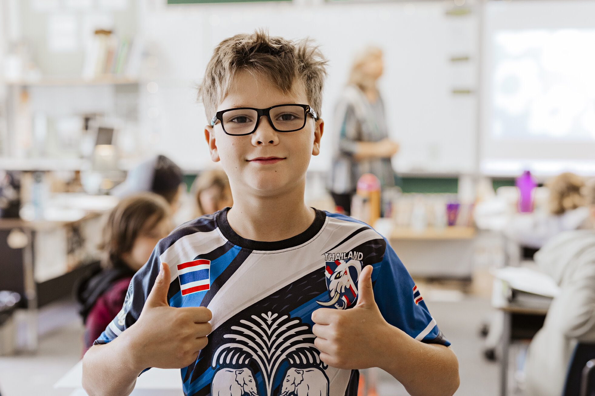 A male ACS middle school student gives a double thumbs up to the camera in class.