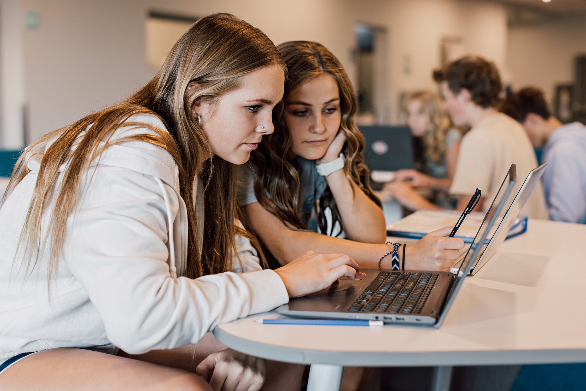 Two female secondary students work at a laptop in the common area.
